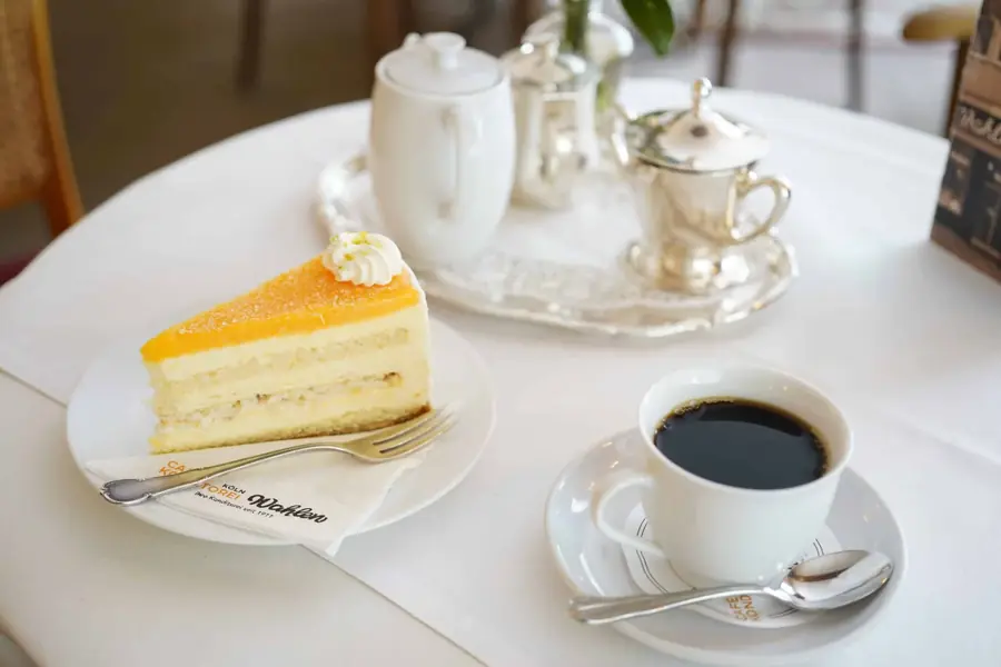 Stück heller Eistorte mit Sahnehaube neben einer Tasse Kaffee
