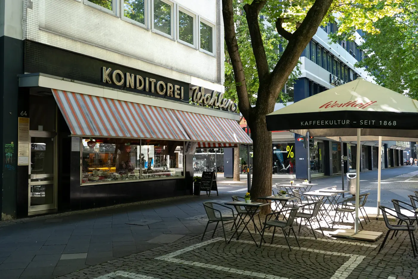 Ladenfront der Café Konditorei Wahlen am Hohenstaufenring mit Markise, Stühlen und Tischen vor dem Haus