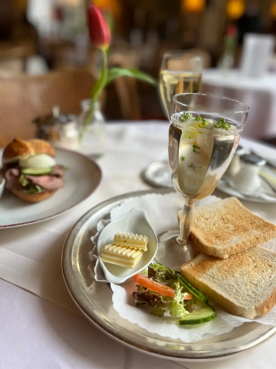 Frühstücksetagere mit belegten Broten, Obst und Sekt auf weißem Tischtuch
