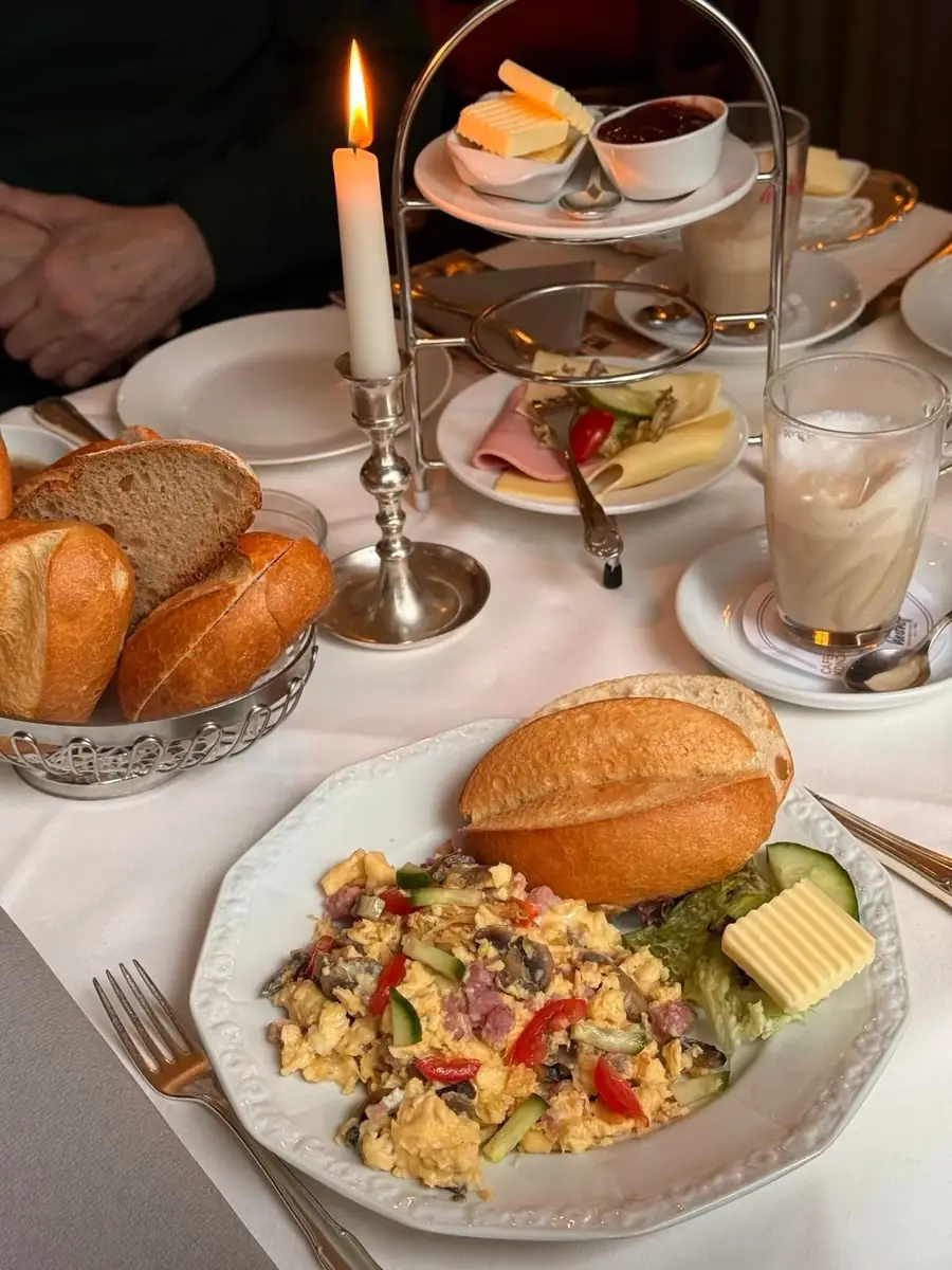 Rührei mit Brötchen, Kerze und Milchkaffee auf weißem Tischtuch