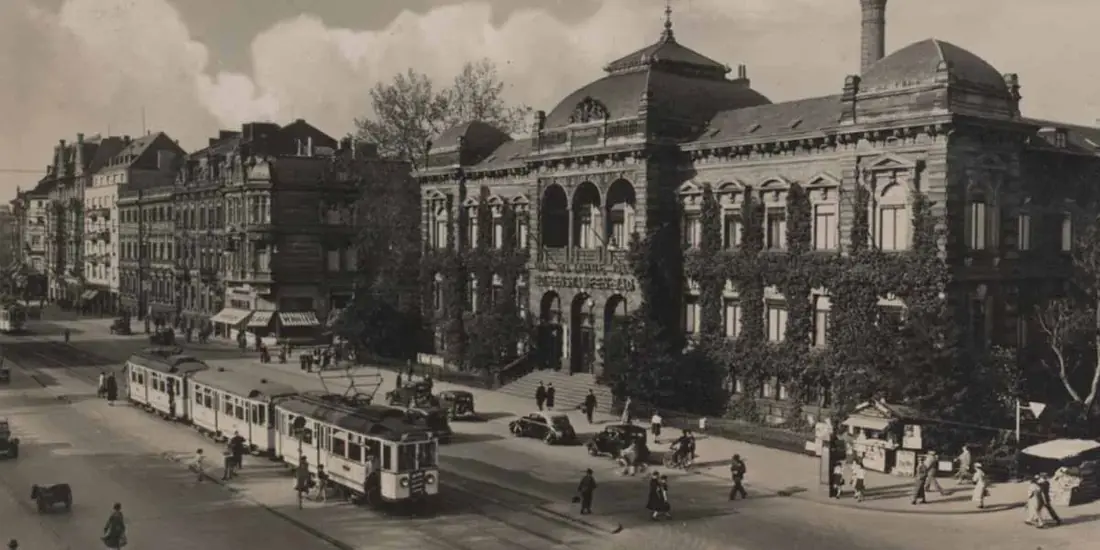 Historische Straßenansicht in Köln mit Straßenbahn vor einem großen Gebäude