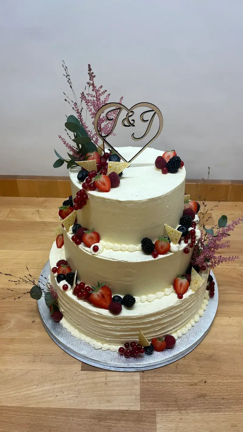 Dreistöckige Hochzeitstorte in Creme mit Beeren und getrockneten Blüten