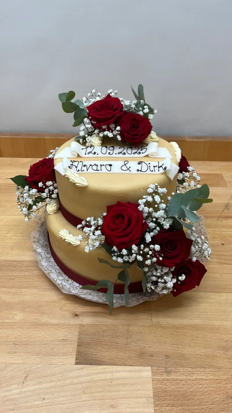 Zweistöckige Hochzeitstorte mit roten Rosen und Namensschild des Brautpaars