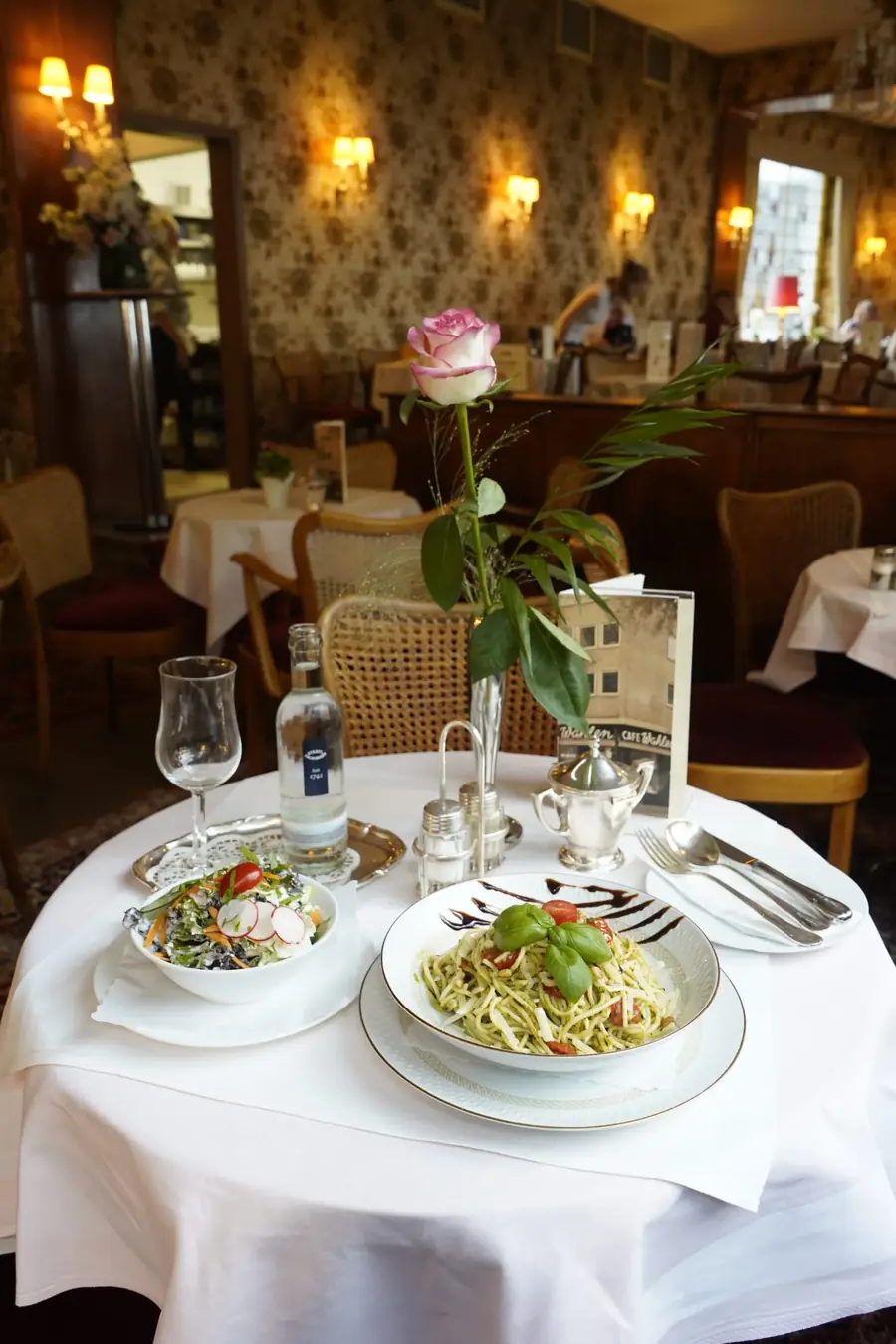 Gedeckter Tisch mit zwei Mittagsgerichten, Weingläsern und Blumenvase im Café Wahlen