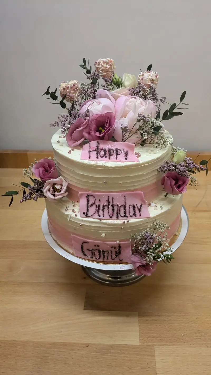 Zweistöckige Geburtstagstorte in Rosé mit Blüten und Happy-Birthday-Schriftzug