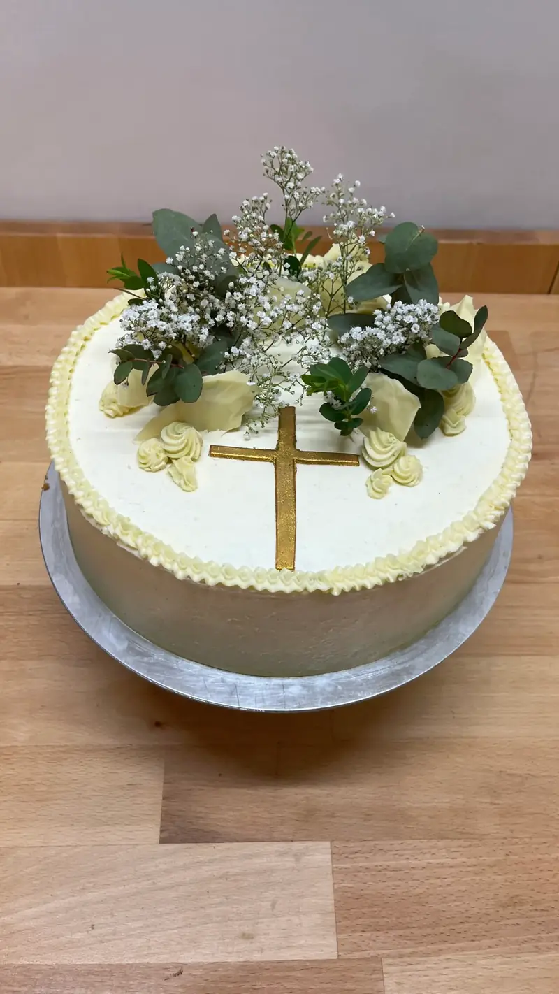 Helle Torte mit goldenem Kreuz, Blüten und Zuckerdekor