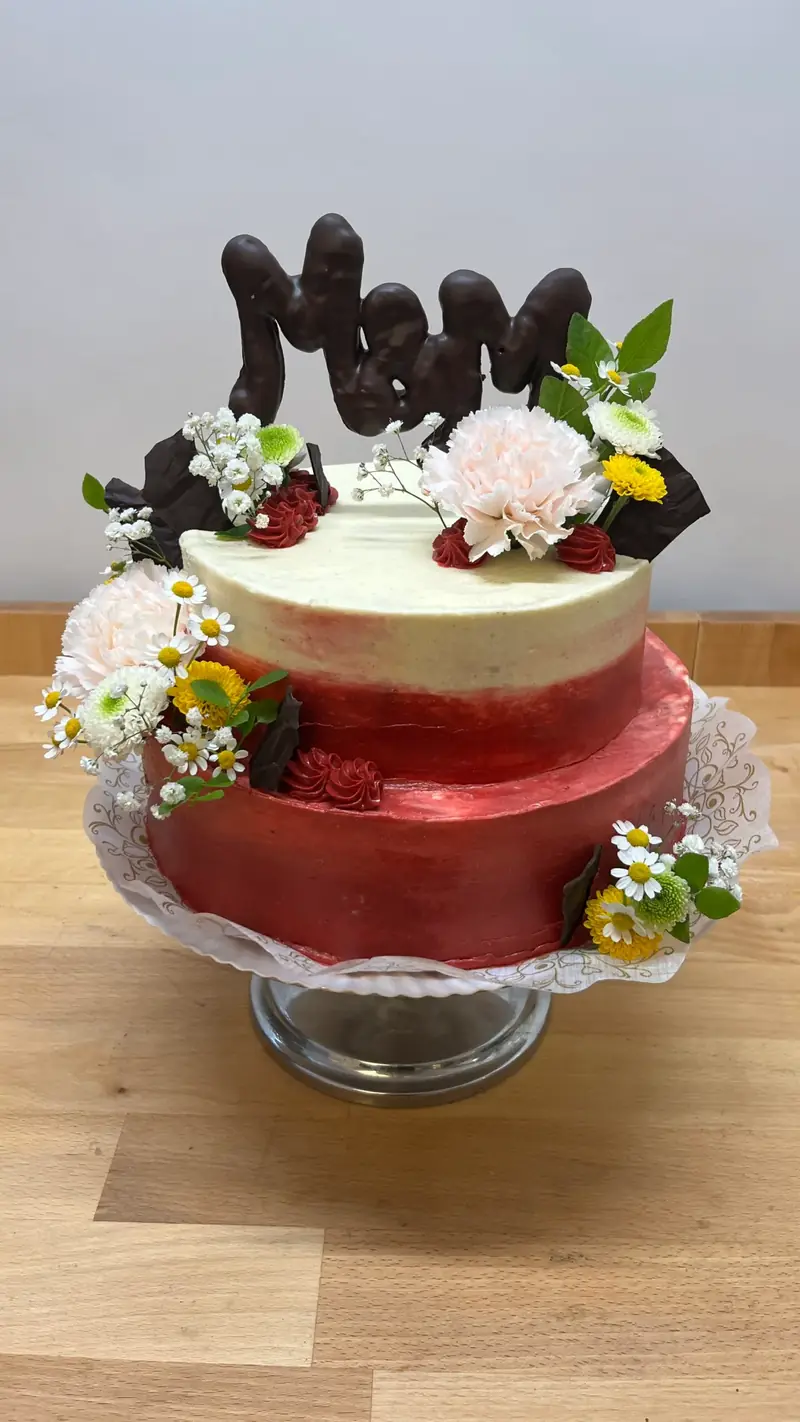 Zweistöckige Torte in Rot und Creme mit Schokoladenbuchstaben und Blüten