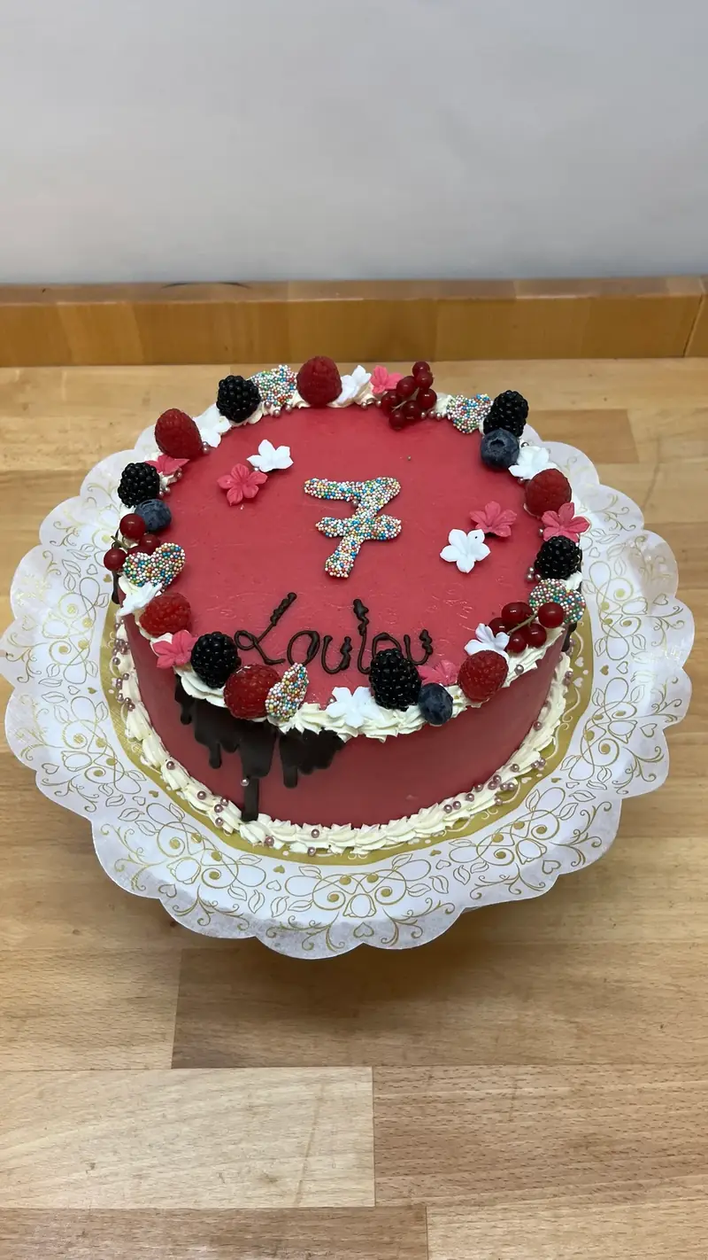 Torte mit dunkelroter Glasur, frischen Beeren und der Zahl Sieben